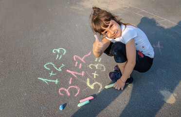 The child solves equations on the asphalt with chalk. Selective focus.