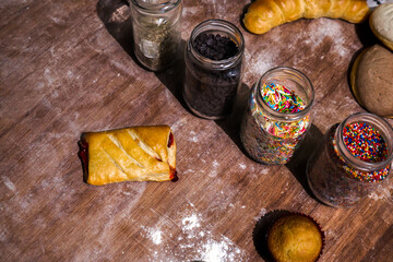 Homemade crusty bread on a wooden table, around glass jars filled with chocolate granules