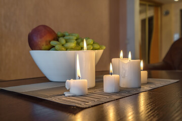 burning candles and a vase with fruit apples and grapes on the table near the lamp