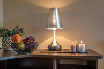 burning candles and a vase with fruit apples and grapes on the table near the lamp