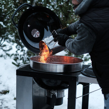 Man with gloves chimney starter barbecue grill in open air at country garden house. Flaming hot red yellow charcoal grill. Concept of country recreation. Winter grilling