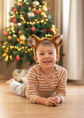 A little boy in a tiger costume lies on the floor against the background of a Christmas tree. Chinese new year symbol