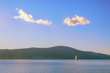 Blue sky and white clouds, white sailboat on blue water. Minimalistic landscape. Travel and vacation concepts.  Montenegro, Kotor Bay