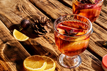 Wine glasses of hot mulled wine with spices, apple and orange on wooden table. Christmas traditional warming drink with cinnamon, cardamom and anise.