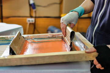 printing on t-shirts by silk screen method in a design studio. male hand with a squeegee....