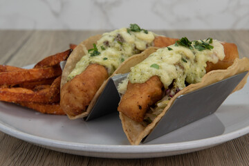 Artistic presentation of crispy deep fried fish tacos covered in melted cheese and served with crunchy french fries