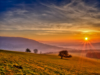 Scenic hilly landscape with solitary trees during sunset, view to the valley, blue sky with high clouds,sun. Autumn evening. White Carpathians mountains,Czech republic. .