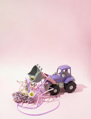 Violet wheel loader bucket full with blooming spring flowers. Minimal love concept. Nature creative idea on pink background. Valentines and womans day idea.