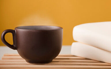 Brown cup of coffee or tea with hot steam, on the table, with books