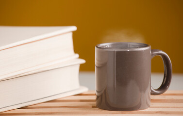 Brown cup of coffee or tea with hot steam, on the table, with book and brown background.