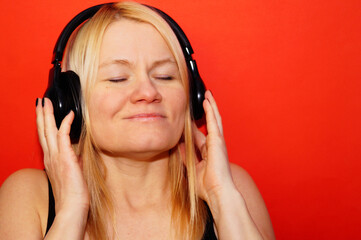 Fototapeta premium A woman listens to music with headphones, enjoying the melody. Portrait of a beautiful woman in close-up without makeup. Eyes closed. Naturalness and a cute face.