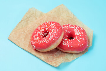 Two donuts with strawberry pink fondant on a piece of parchment on a turquoise background. Sweet...