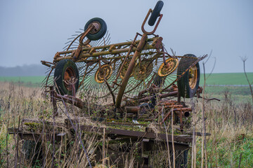 an old abandoned, rusting, overgrown farm equipment machinery rake and thresher tractor attachment,...