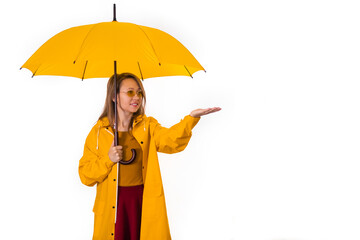 A smiling girl in a yellow raincoat stands under an umbrella and stretches out her hand in the rain