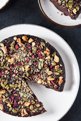 Beet and Kale Chocolate cake topped with pecans, pumkin seeds on a white plate placed on a black...