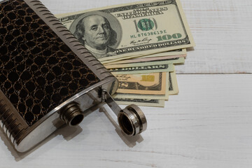 Metal flask and dollars close-up on white painted wooden table