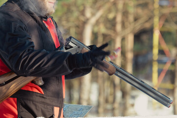 Hunter in camouflage with rifle in winter forest. Hunt concept. Man securing a reserve, on a snowy day. Hunter takes aim from a gun in the snowy forest