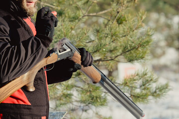 Hunter in camouflage with rifle in winter forest. Hunt concept. Man securing a reserve, on a snowy day. Hunter takes aim from a gun in the snowy forest