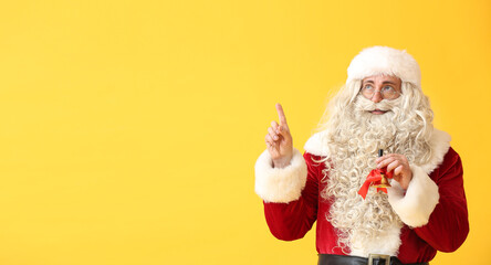 Fototapeta na wymiar Santa Claus with Christmas bell pointing at something on yellow background with space for text