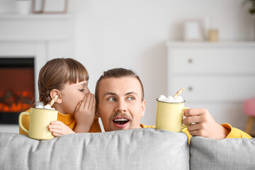 Happy daughter and father with cups of hot cocoa behind sofa at home