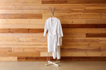 Rack with white bathrobes near wooden wall