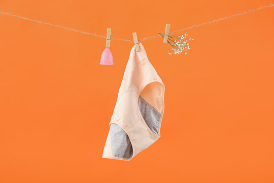 Period panties, menstrual cup and gypsophila flowers hanging on rope against color background