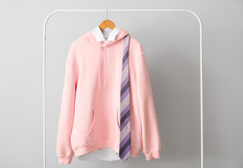 Rack with stylish pink hoodie, shirt and necktie near light wall