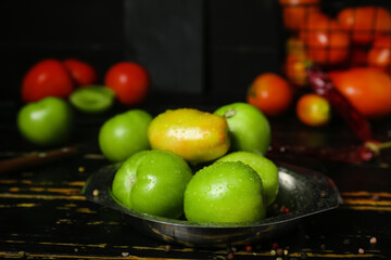 Bowl of fresh green tomatoes with water drops on dark wooden table