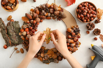 Woman making beautiful acorn wreath on light background