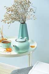 Tea pot and cup of hot beverage on table near blue wall