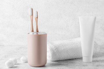 Holder with wooden toothbrushes, paste and towel on light background