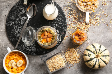 Jar and pot of tasty oatmeal with pumpkin on grunge background
