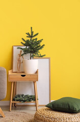 Small Christmas tree in flowerpot on table near color wall