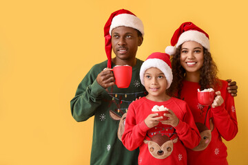 African-American family in Santa hats and with cups of tasty hot chocolate on color background