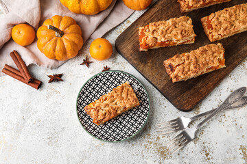 Plate and wooden board with pieces of tasty pumpkin pie on light background