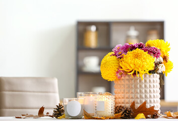 Burning candles in holders, vase with beautiful Chrysanthemum flowers and autumn decor on table in room