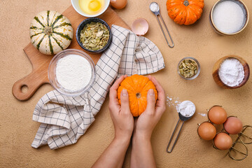 Female hands with fresh ingredients for preparing pumpkin pie on beige background