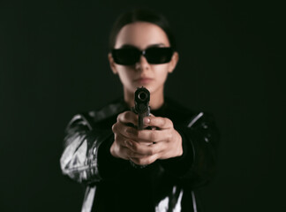 Woman with gun dressed in matrix style on dark background