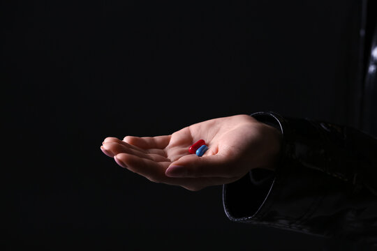 Female hand with blue and red pills on dark background. Concept of choice