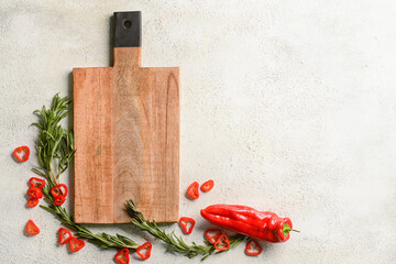 Wooden cutting board with chili pepper and rosemary on white background