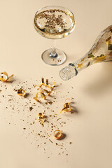 Glass of champagne, bottle and golden confetti on color background