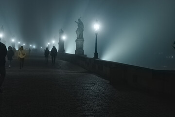 Fototapeta na wymiar Street lamps and light from them on the old stone Charles Bridge in the night fog and silhouettes of figures