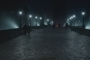 Street lamps and light from them on the old stone Charles Bridge in the night fog and silhouettes of figures © svetjekolem