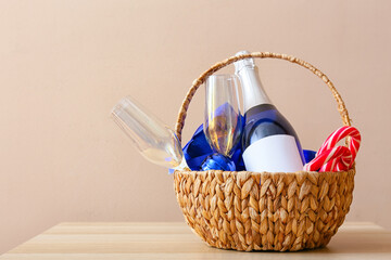 Basket with bottle of champagne, glasses and candy canes on table near color wall