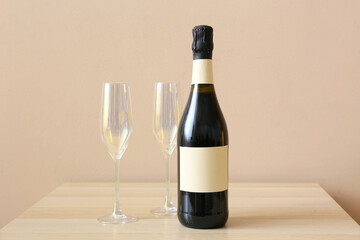 Bottle of champagne and glasses on wooden table near color wall