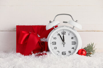 Alarm clock and Christmas gift on snow against light wooden background
