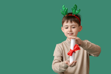 Funny little boy with reindeer horns and scroll on color background