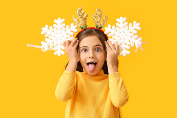 Funny little girl with reindeer horns and snowflakes on color background