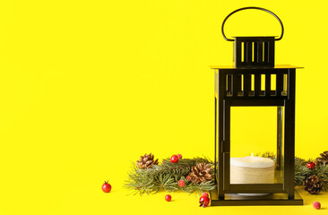 Fototapeta premium Black metal christmas lantern with burning candle, pine cones, and red berries on bright yellow background