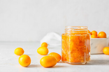 Jar of tasty kumquat jam and fresh fruits on light background